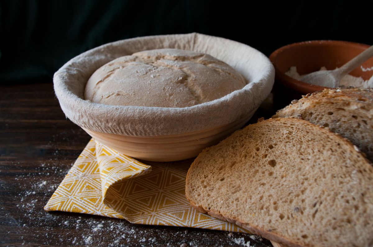 Bread dough in bowl next to slices of bread on brown table 