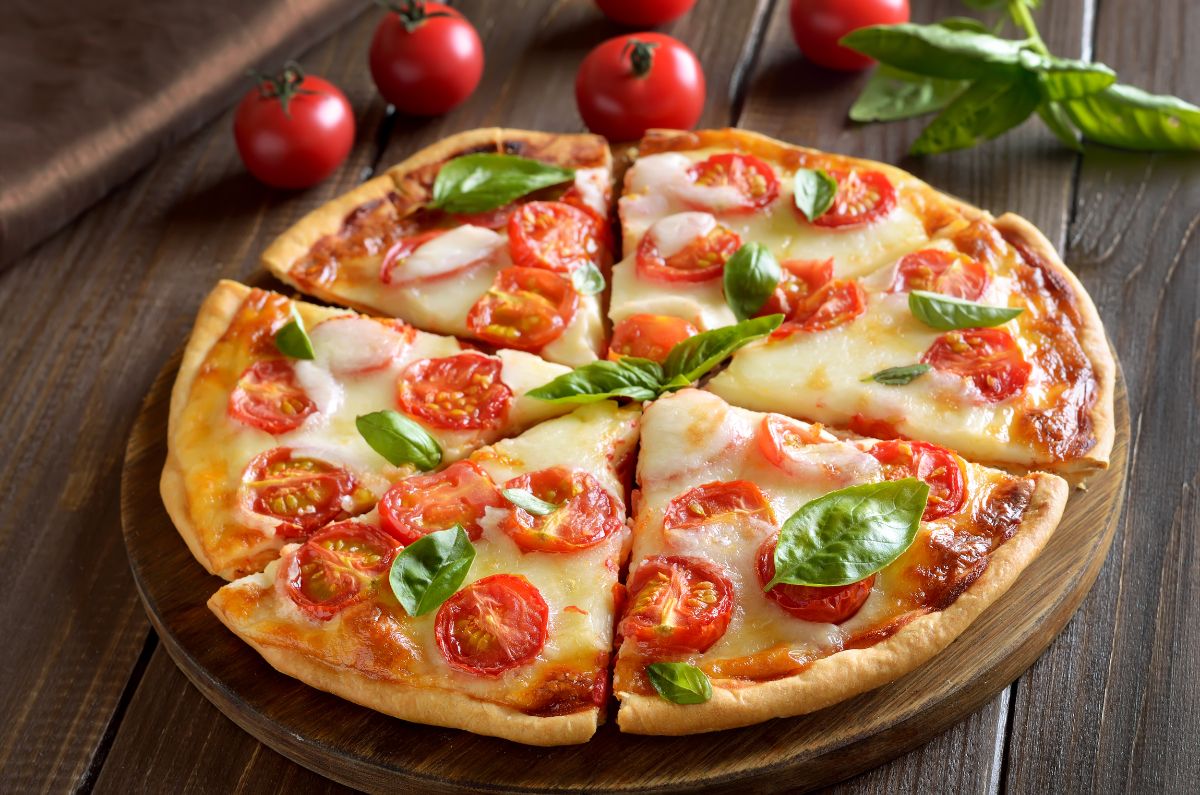 Sliced pizza on wooden pad with herb and tomatoes on wooden table