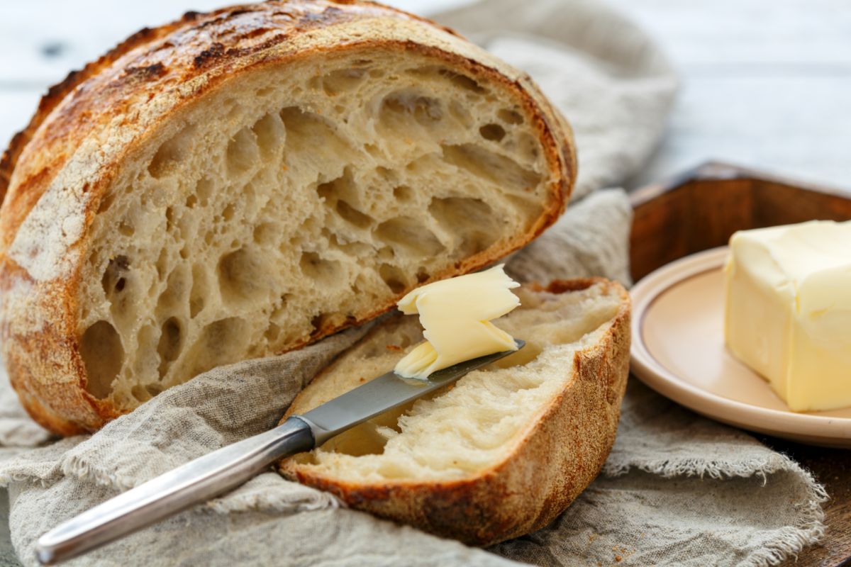 Partialy sliced loaf of sourdough bread with butter and knife on cloth wipe