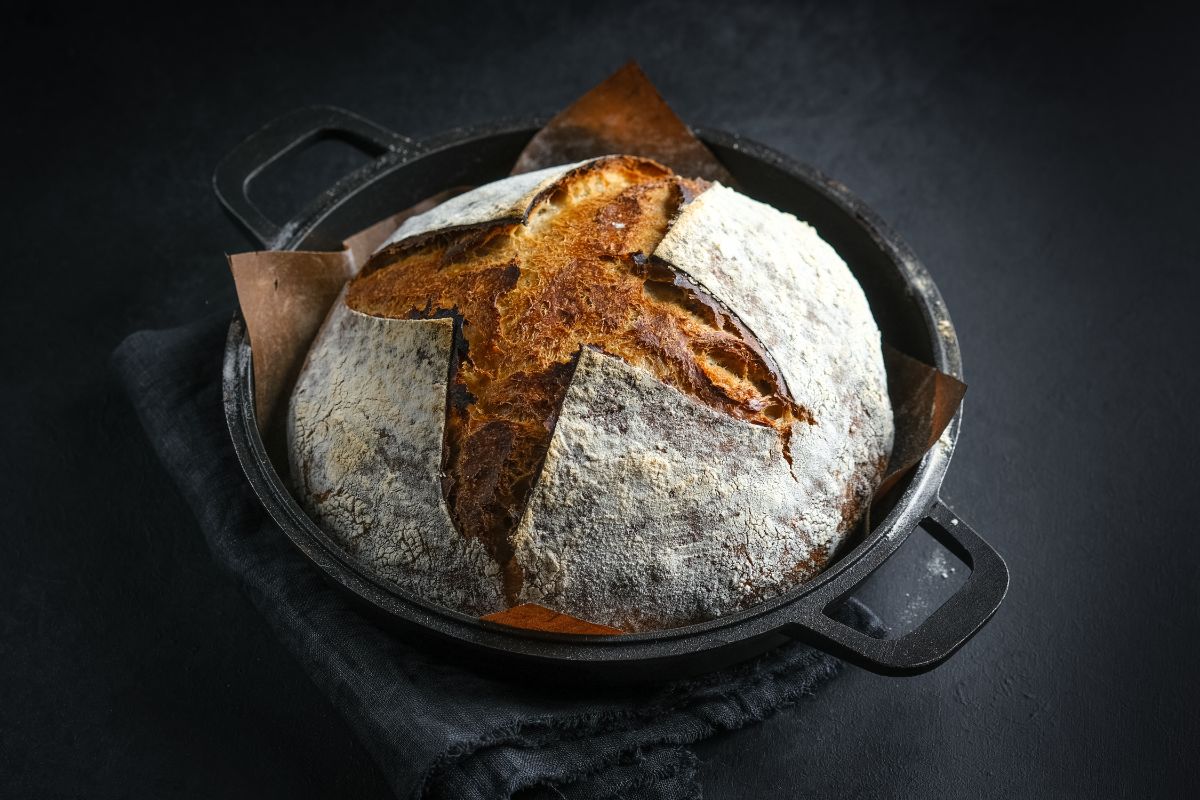 Sourdough loaf of bread in dutch oven on black table and cloth wipe