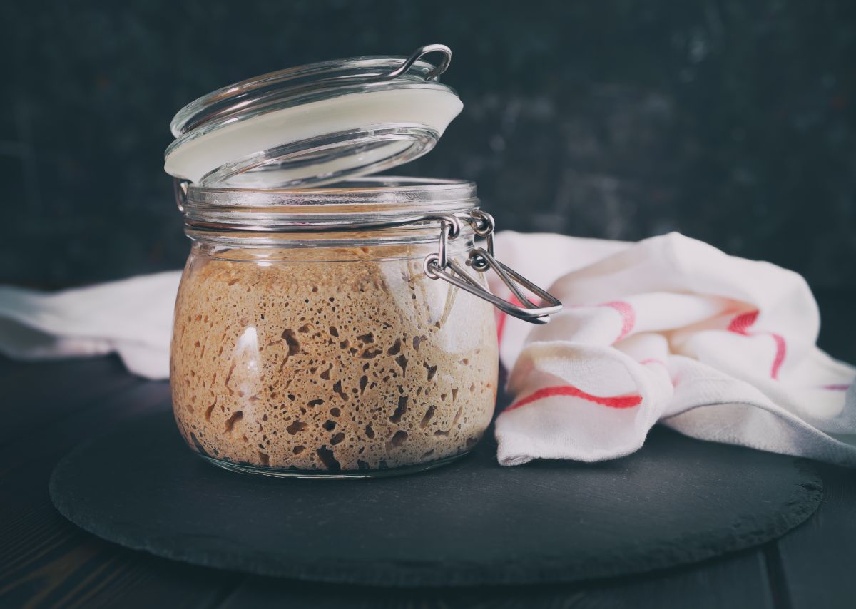 Sourdough starter in glass jar on black pad with cloth  wipe on table