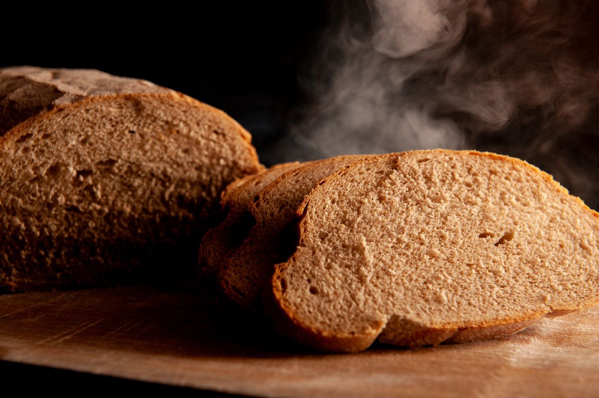 Steaming sliced loaf of bread on wooden pad