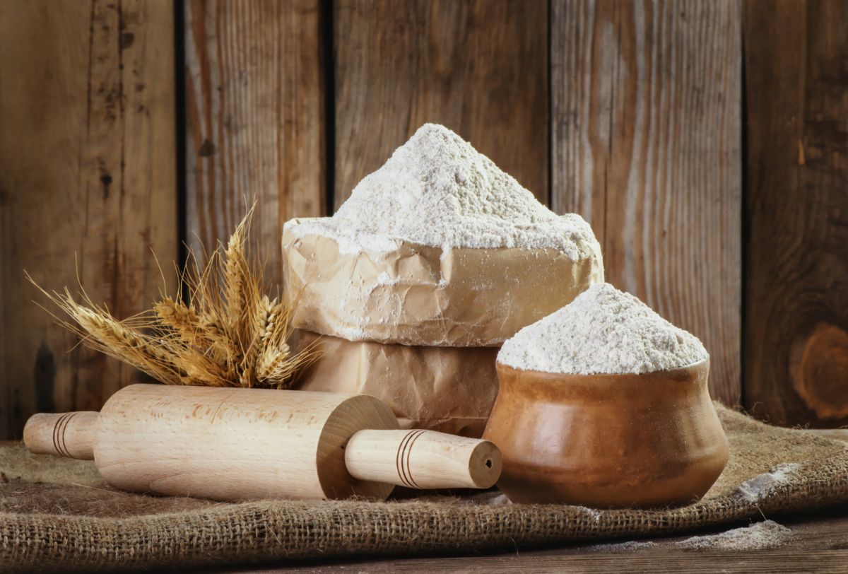 Wheat flour in paper bag and brown bowl on cloth bag with wooden kitchen roller and stalks of wheat