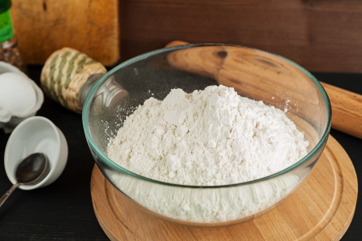 White flour in glass bowl on wooden cutting board