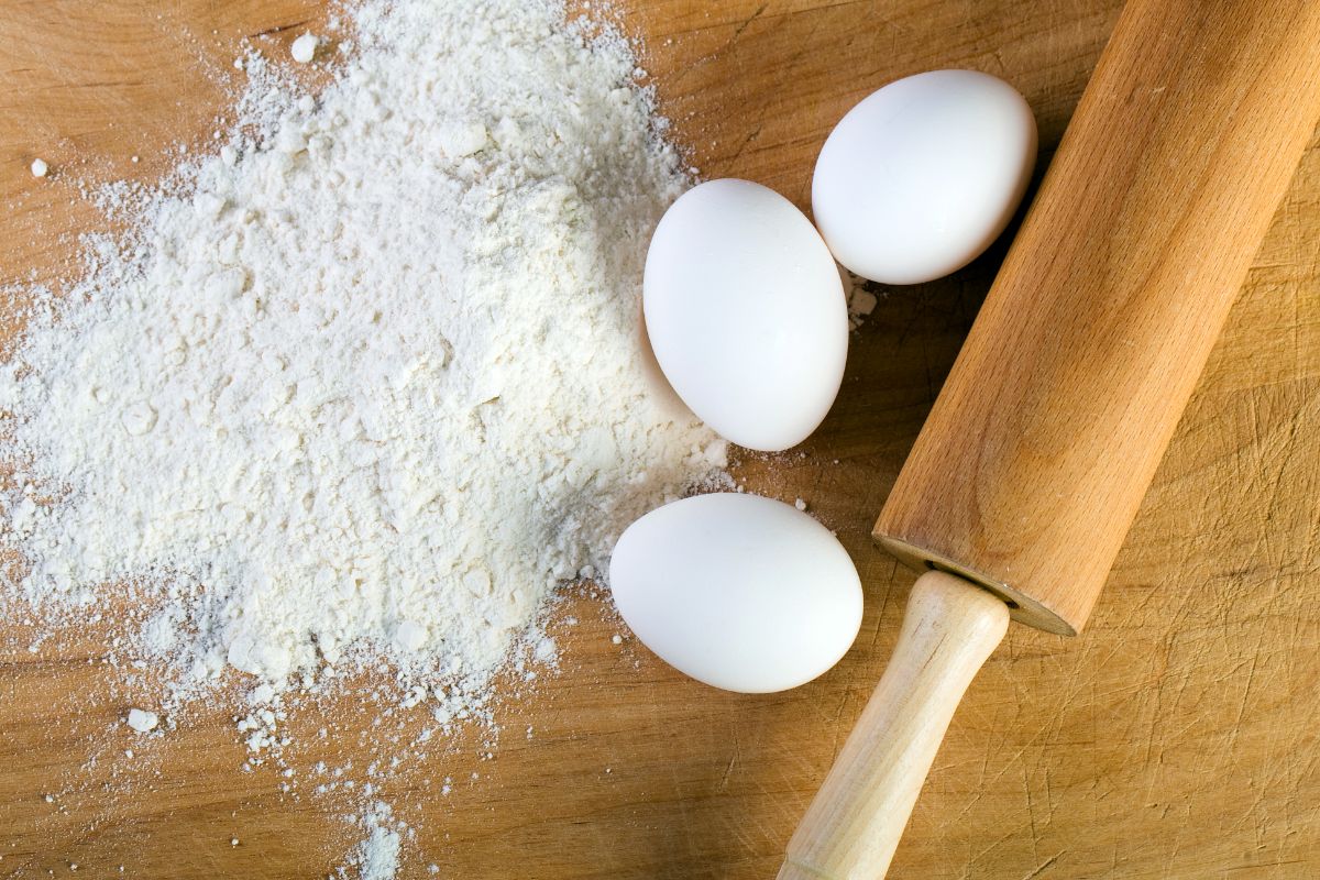 White flour with eggs and wooden roller on wooden pad