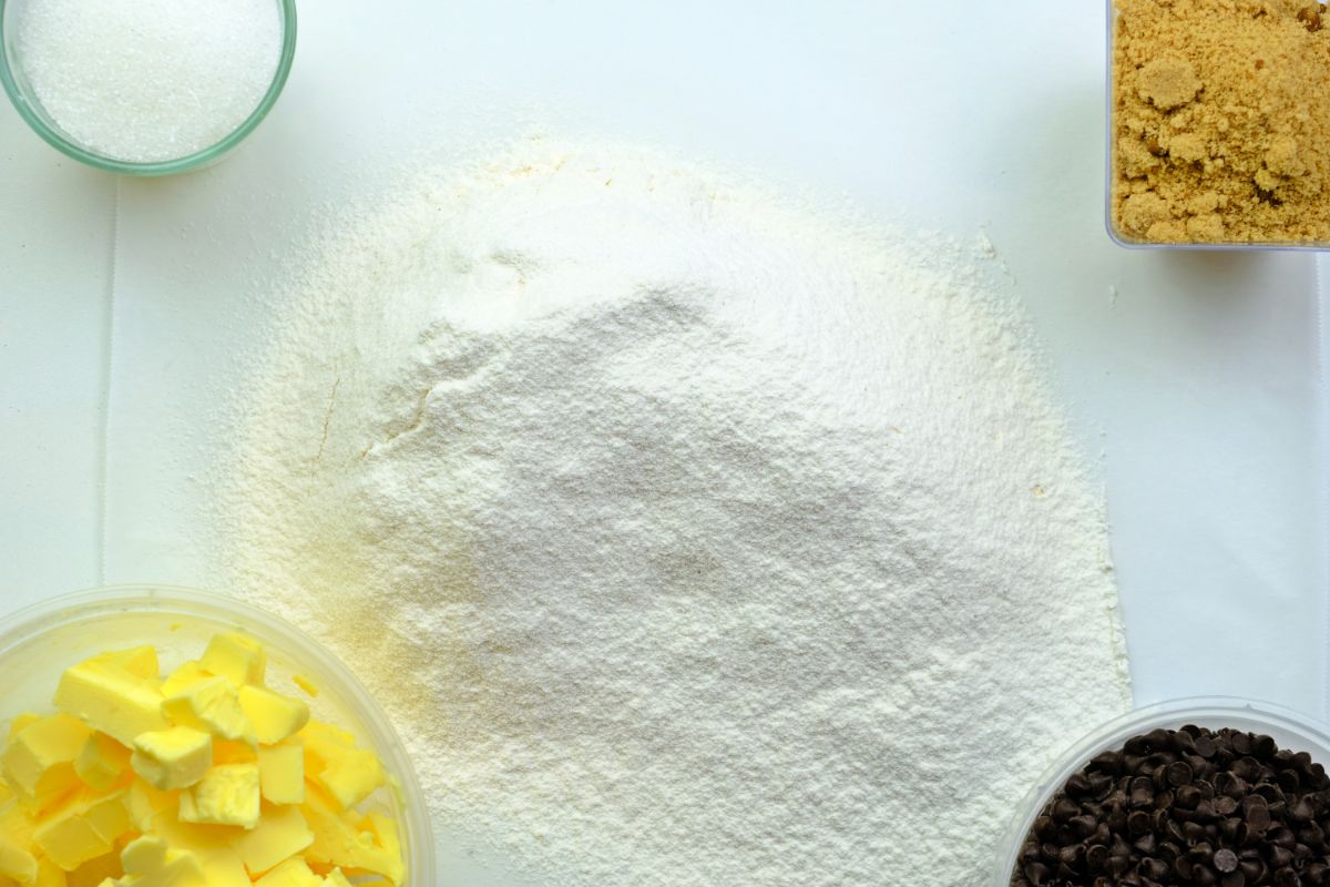 Pile of white flour with ingredients in glass bowl on white table