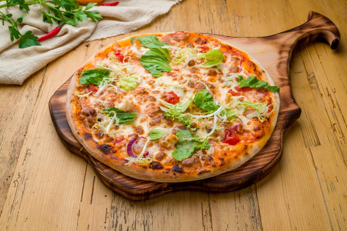 Freshly baked pizza on wooden pad on wooden table