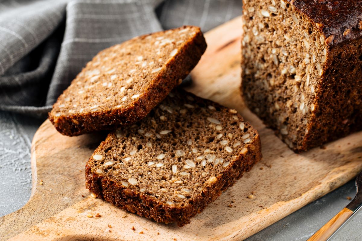 Partially sliced wholegrain loaf of bread on wooden cutting board