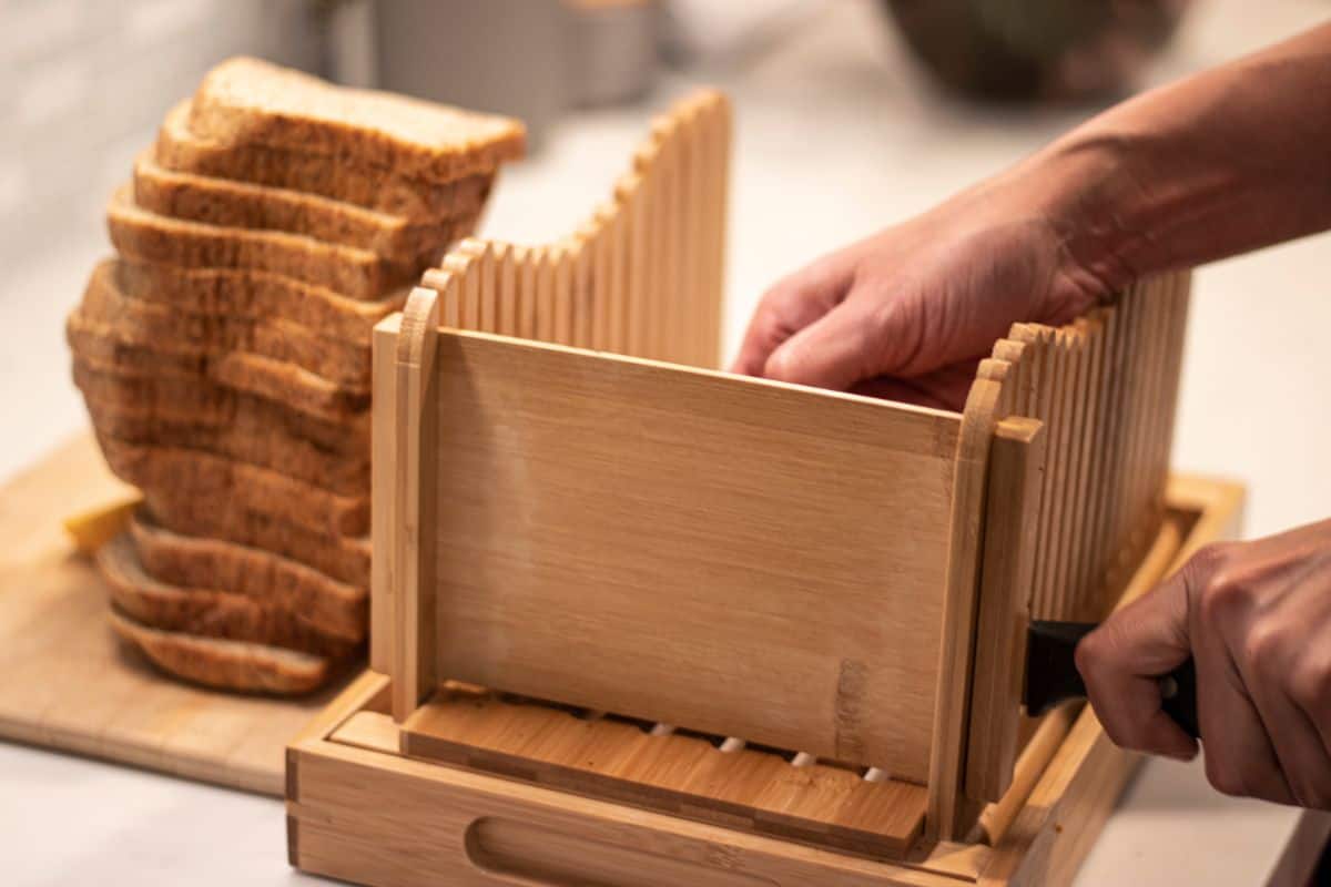 Wooden bread slicer, man holding knife, slices of bread on wooden pad