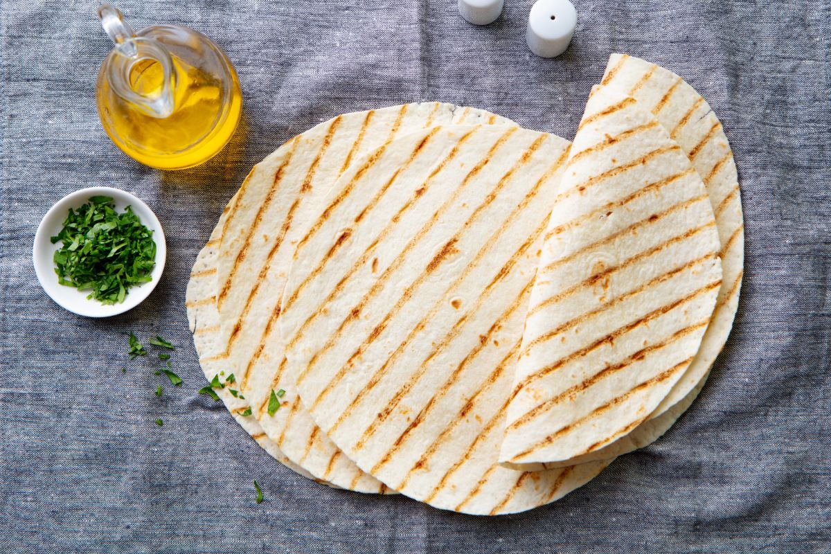 Pile of wraps on gray table cloth with glass pitcher and bowl of herbs